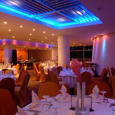 Decapolis Hotel פנמה סיטי מתקנים תמונה The image shows an elegant restaurant interior. The dining area features round tables covered with white tablecloths, and each table is set with glassware and napkins. The chairs are draped in orange fabric, contributing to a warm and inviting atmosp
