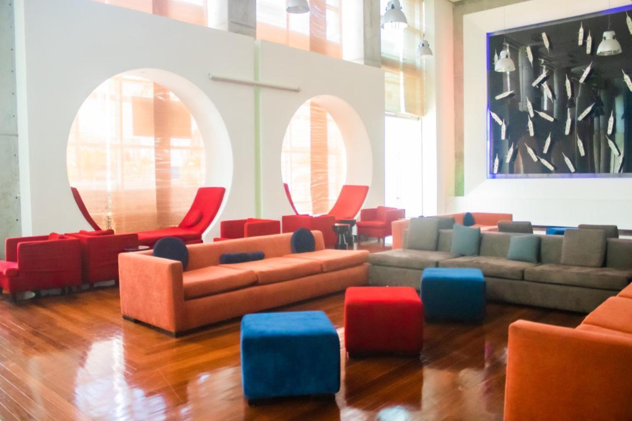Decapolis Hotel פנמה סיטי מראה חיצוני תמונה The photo depicts a modern and stylish lounge area. It features a combination of colorful seating arrangements, including a long, orange sofa and various cubes in blue and red, creating a vibrant atmosphere. There are also two red lounge chairs with 