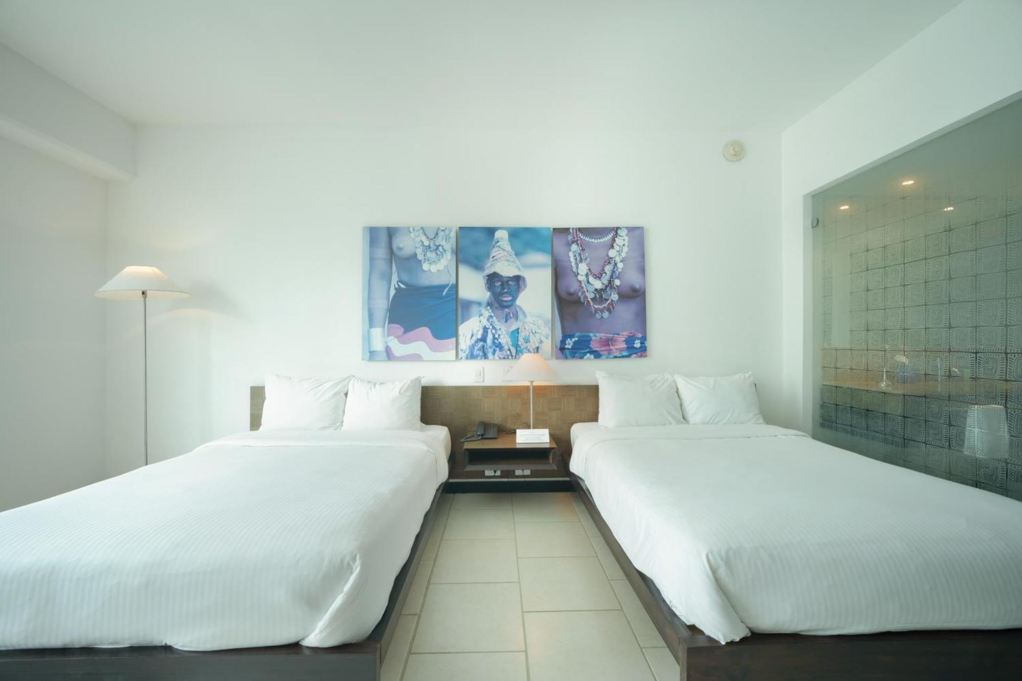 Decapolis Hotel פנמה סיטי מראה חיצוני תמונה The photo shows a modern hotel room featuring two double beds with white bedding. The walls are painted a light color, contributing to a clean and minimalist aesthetic. Above the beds, there is a large piece of artwork that displays a colorful design