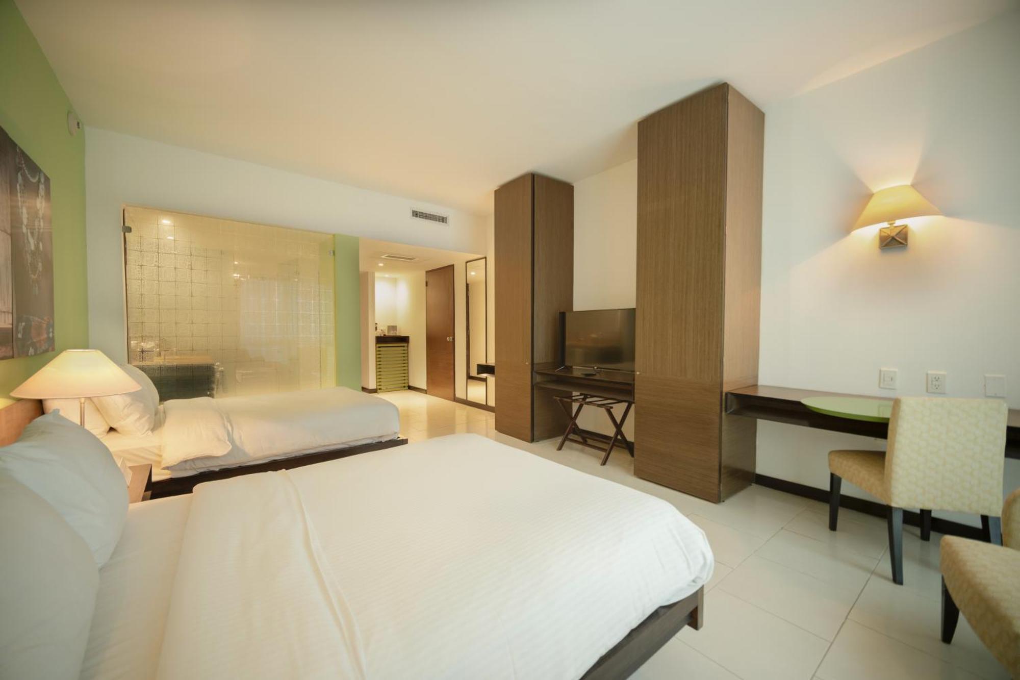 Decapolis Hotel פנמה סיטי מראה חיצוני תמונה The photo shows a modern hotel room featuring two beds with white bedding. There is a large window allowing for natural light, and one wall is occupied by built-in cabinets and a flat-screen TV. A small desk with a chair is positioned near the TV, an