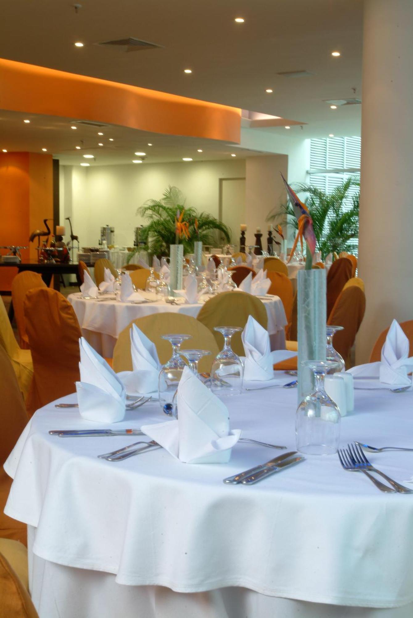 Decapolis Hotel פנמה סיטי מסעדה תמונה The photo shows a well-set dining area in a restaurant. There are elegantly arranged tables covered with white tablecloths, and each table features neatly folded napkins. Glassware, including wine glasses and water glasses, is placed on the tables. T