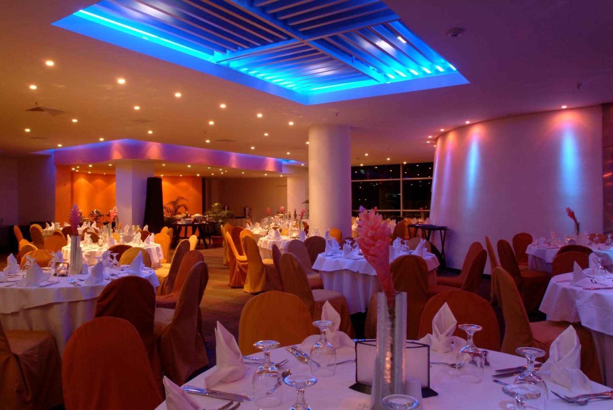 Decapolis Hotel פנמה סיטי מתקנים תמונה The image shows an elegant restaurant interior. The dining area features round tables covered with white tablecloths, and each table is set with glassware and napkins. The chairs are draped in orange fabric, contributing to a warm and inviting atmosp