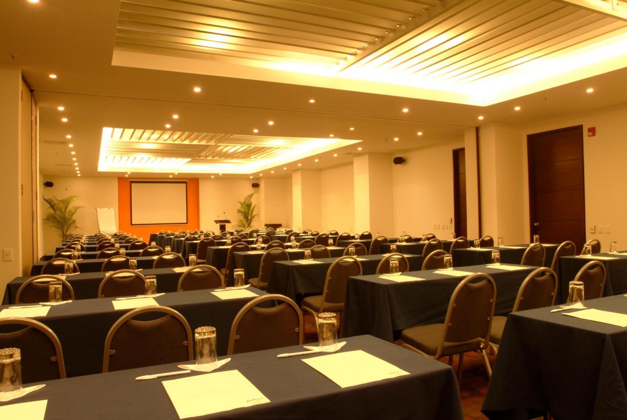 Decapolis Hotel פנמה סיטי מראה חיצוני תמונה The photo shows a conference or meeting room set up for an event. There are multiple rows of tables arranged with dark-colored tablecloths. Each table is equipped with a piece of paper or a notepad, and there are glass jars or cups placed on the tabl